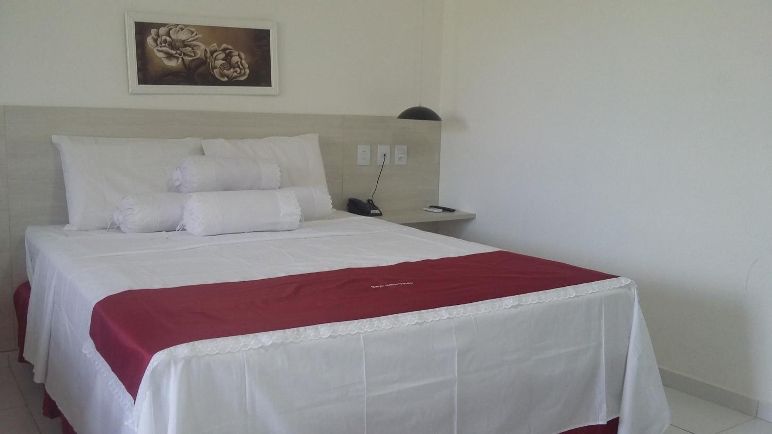 Ein Hotelzimmer mit einem ordentlich bezogenen Bett, einem Nachttisch mit Lampe und einem Bild an der Wand.