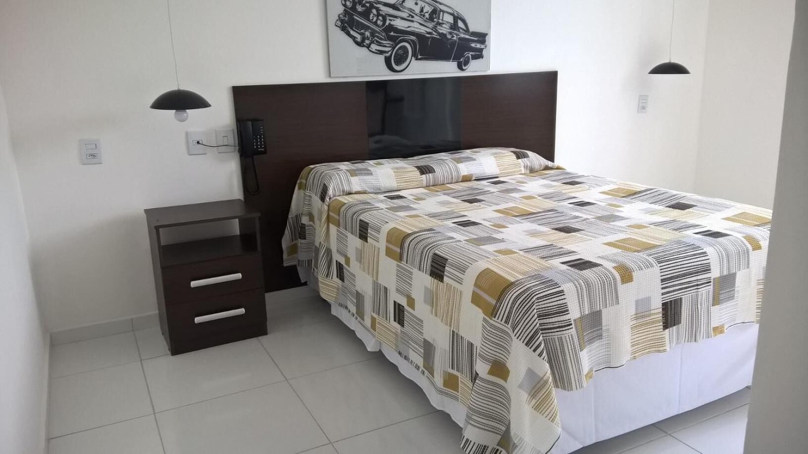 A neatly arranged bedroom with a bed, bedside tables, a phone, and a wall-mounted artwork.