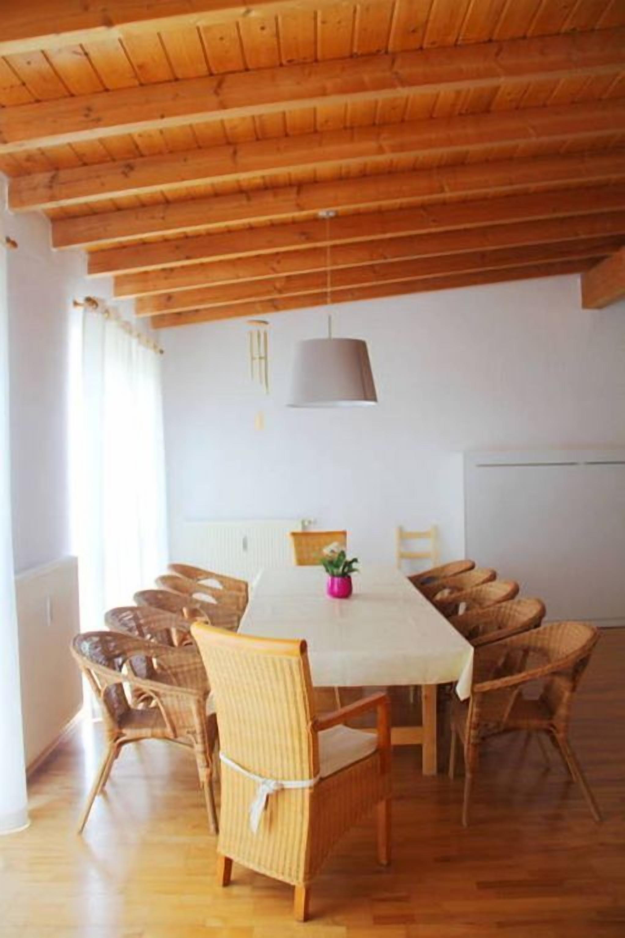 A dining area with a wooden ceiling, a white table, and wicker chairs.