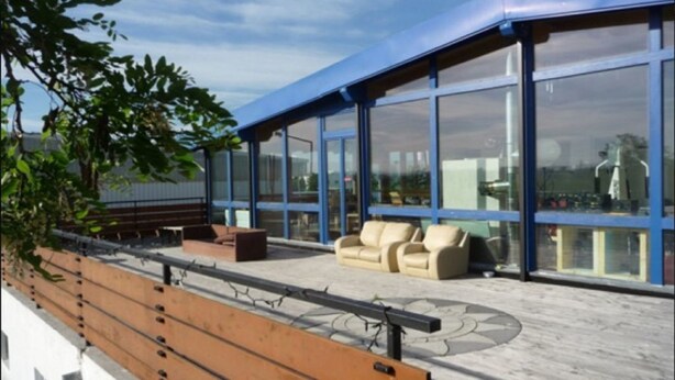 A rooftop terrace with a wooden bench, outdoor seating, and large windows offering views of the city. - Haus EMG Hockenheim (Hockenheim)