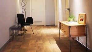 A narrow hallway with wooden flooring and a sloped ceiling. There are two chairs, a desk with a lamp, and a framed picture on the desk. - Haus EMG Hockenheim (Hockenheim)