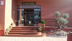 Un edificio in mattoni con un'insegna che riporta la scritta “CAFETERÍA” sopra l'ingresso. Si raggiungono i gradini d'accesso, e vasi con piante sono disposti lungo la scalinata.