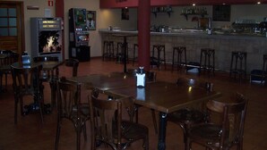Un interno ristorante con tavoli e sedie in legno, una zona bar e macchinette arcade.