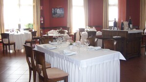 Una sala ristorante con diversi tavoli apparecchiati, ognuno con tovaglie bianche e bicchieri da vino.
