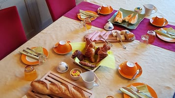Een ontbijttafel gedekt met croissants, brood, jam en gebak.