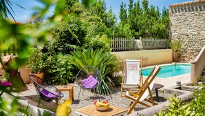 A poolside area with a wooden table, two chairs, a fruit bowl, and lush greenery. - Villa Limonade (Olonzac)
