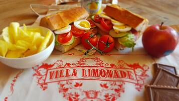 Un tavolo con un panino, pomodori, cetrioli, uova e una ciotola di ananas.