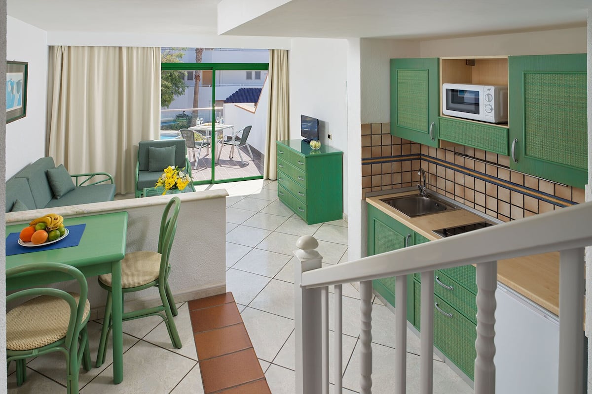 A modern kitchen with green cabinets, a microwave, and a dining area with a table and chairs.