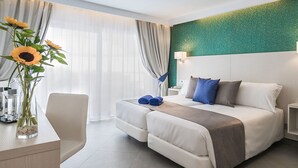 A hotel room with a bed, bedside tables, a desk with a vase of flowers, and a view of the outdoors. - Aparthotel Esquinzo Y Monte Del Mar (Pajara)
