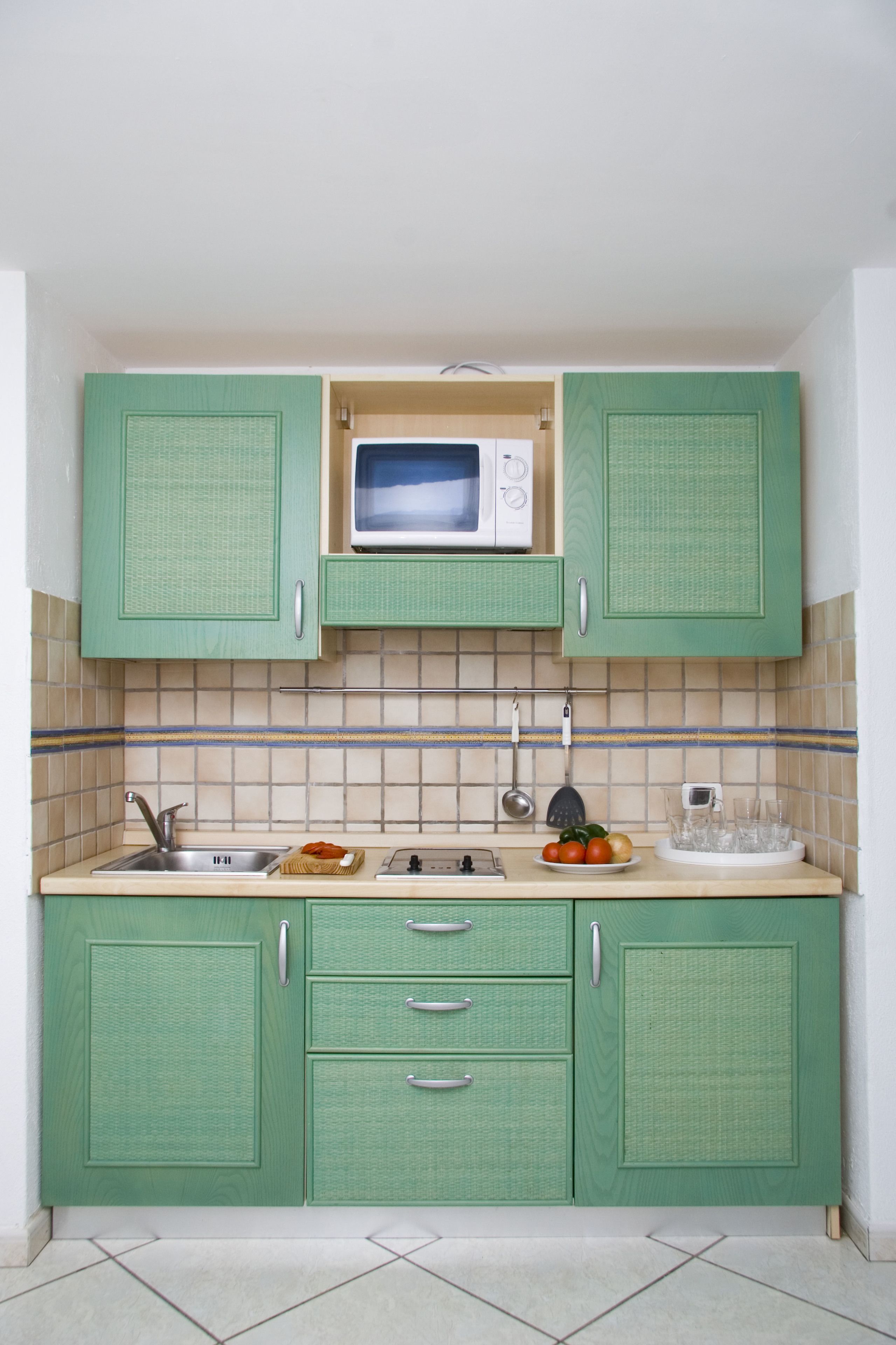 Une cuisine compacte avec des meubles de couleur verte, un four à micro-ondes, un évier et un pare-feu en carreaux.