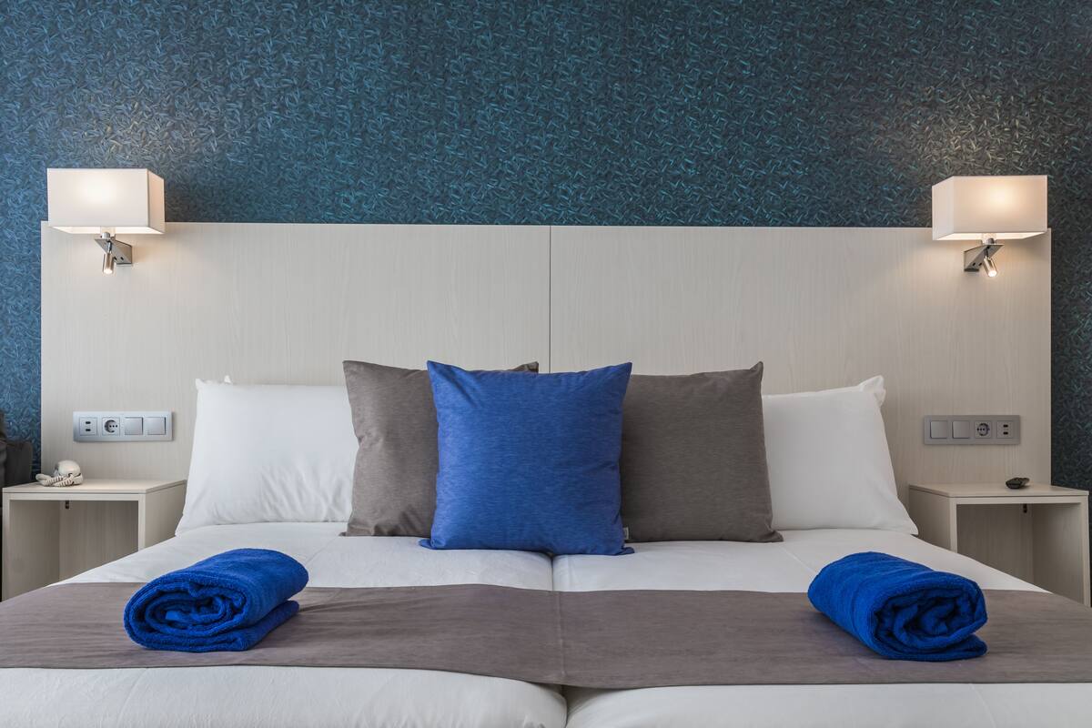 A hotel room with a large bed, two nightstands, and wall-mounted lamps.