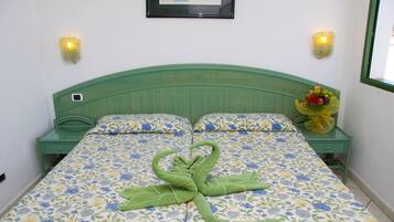 Una cama con una colcha floral, un cabecero verde y un ramo de flores sobre una mesita de noche.