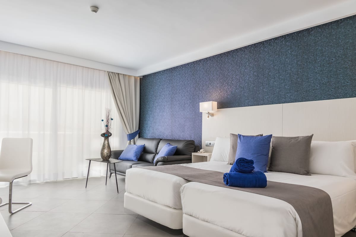 A modern hotel room with a large bed, a sofa, a small table, and a chair.