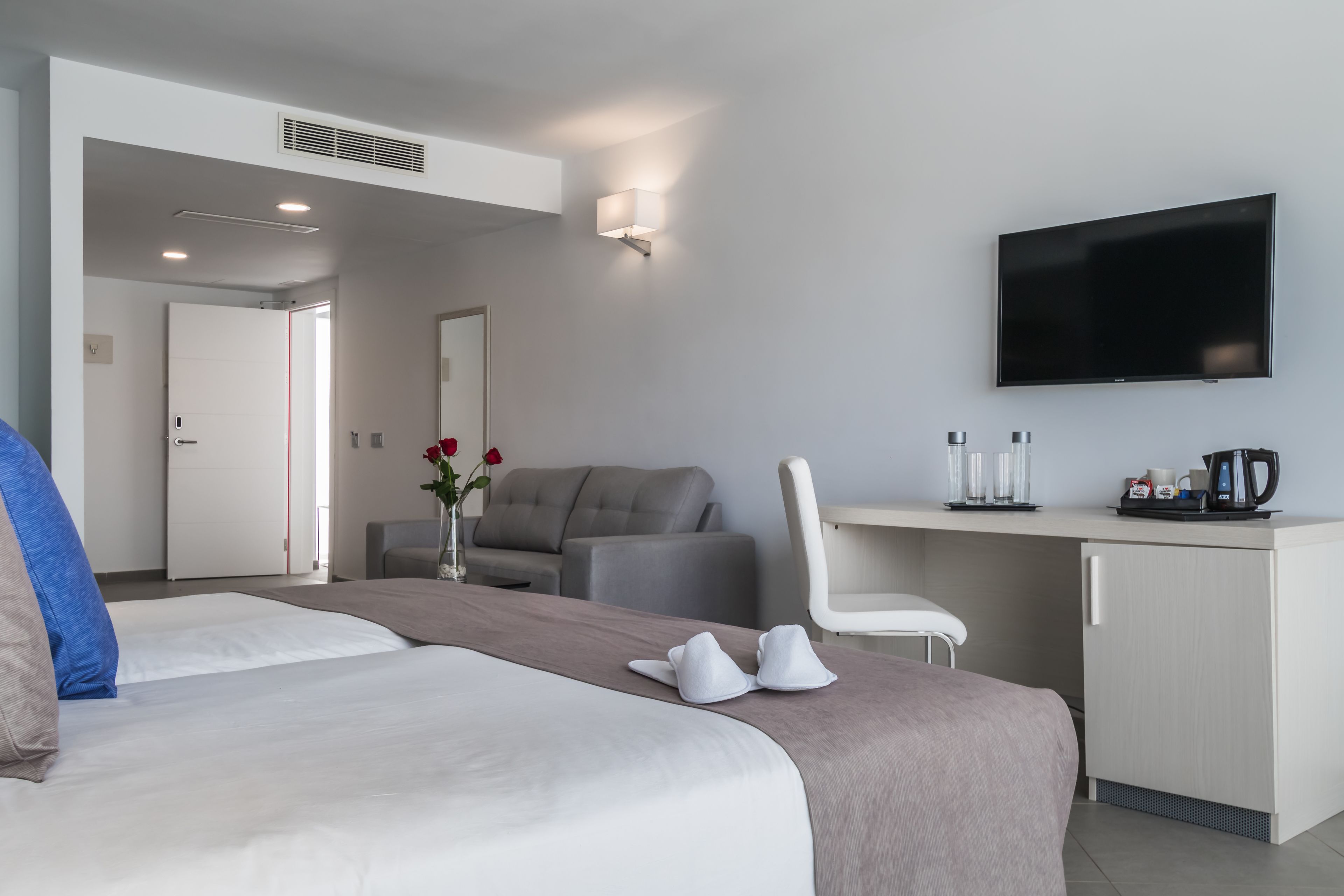 A hotel room with a bed, a desk, a television, and a seating area.