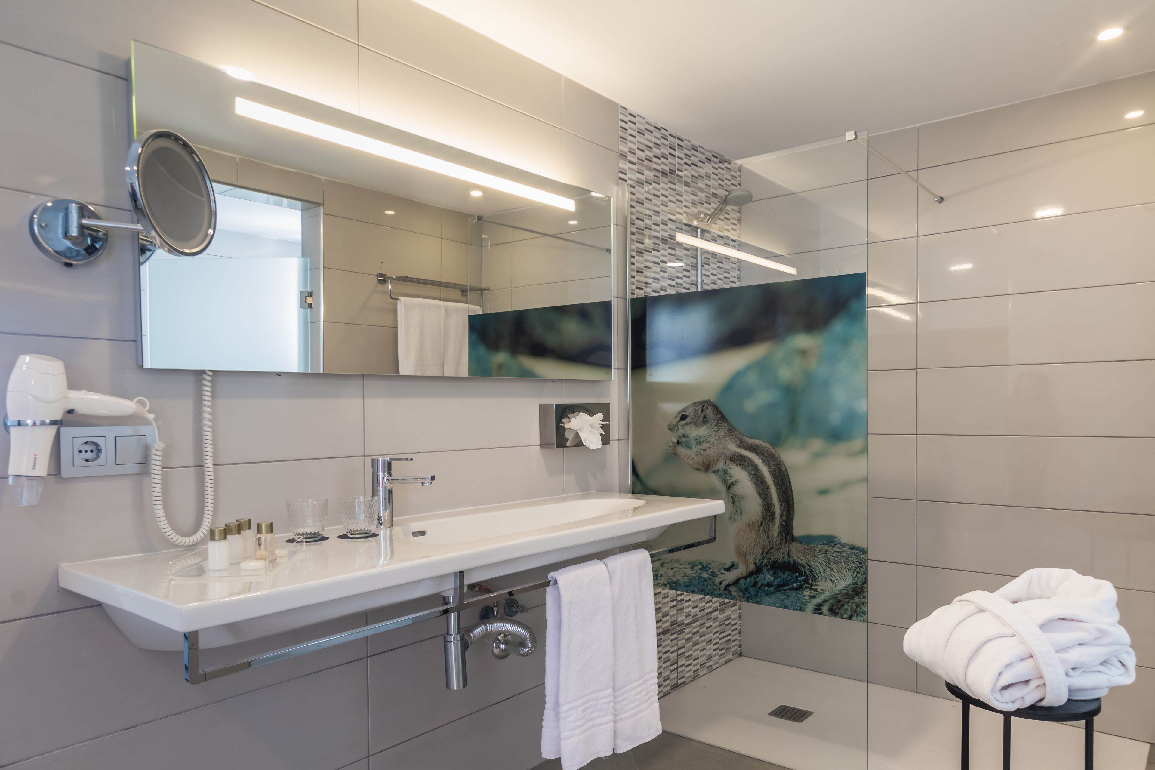 A modern bathroom with a large mirror, white sink, and a shower area.