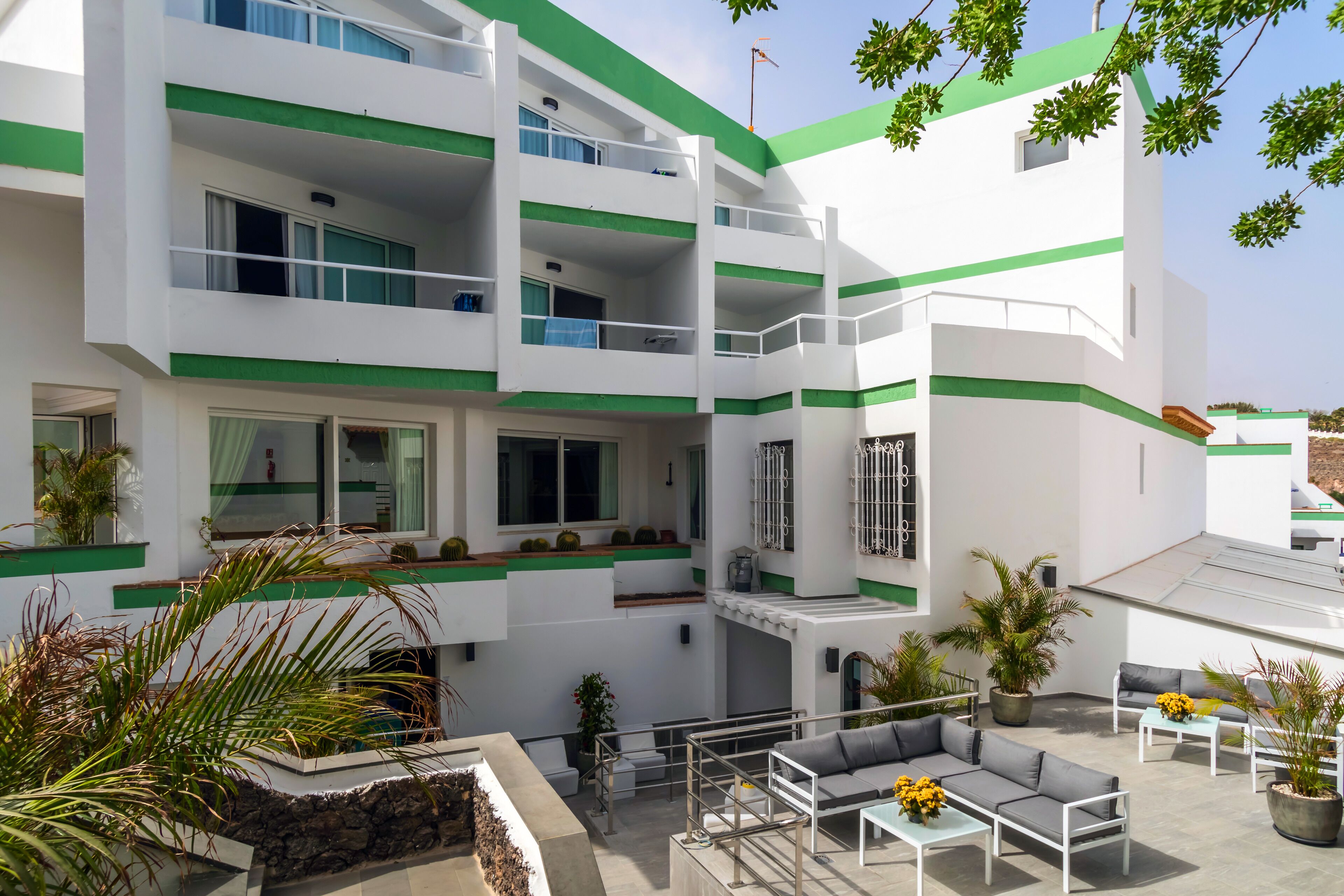 Un hotel de varios pisos con balcones, mobiliario exterior y plantas en macetas.