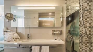 Une salle de bain moderne avec un grand miroir, un lavabo et un espace douche.