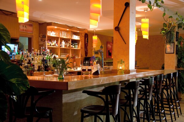 A bar area with a long counter, multiple shelves of bottles, and several chairs.