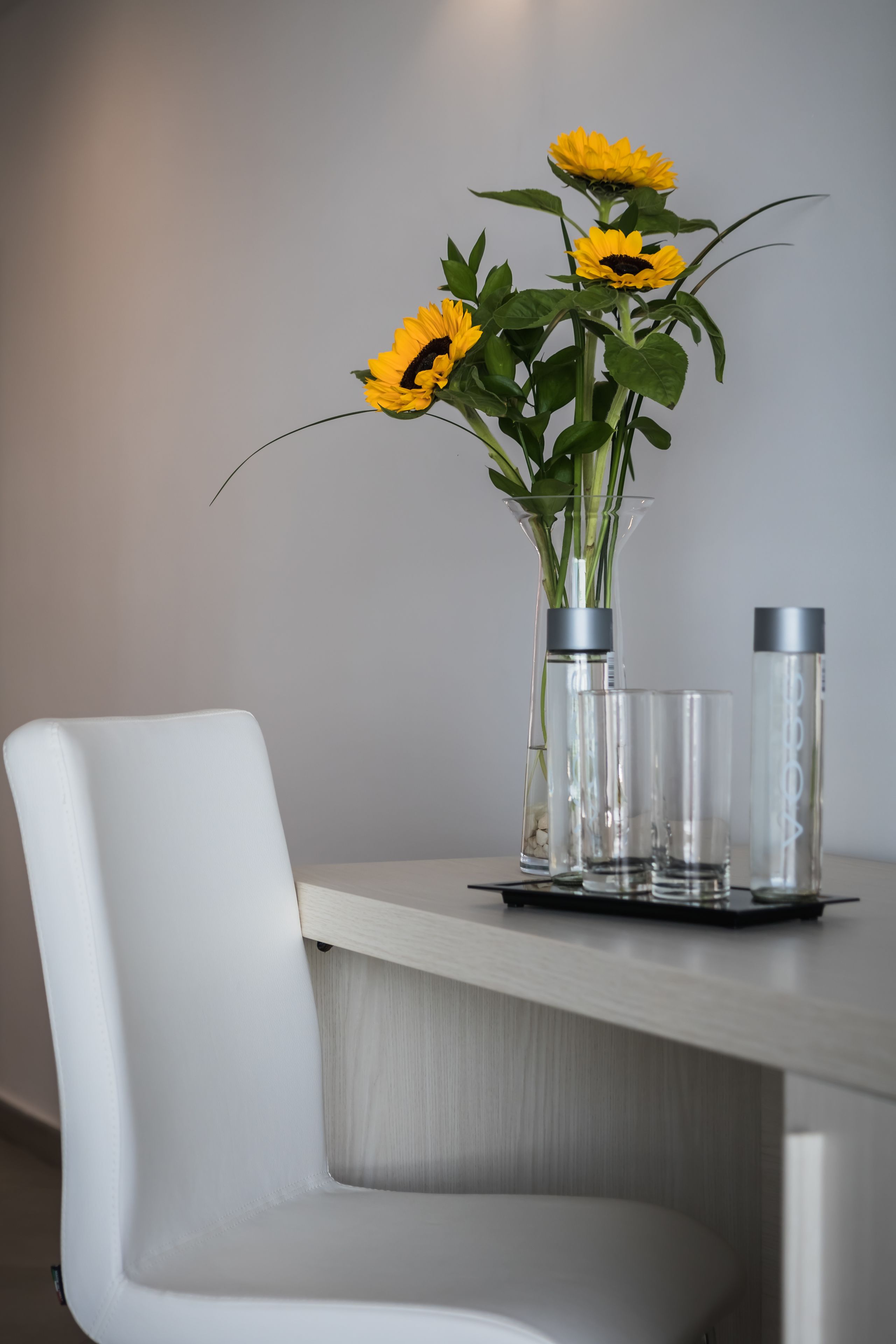 A dining table with a vase of sunflowers, a glass, and a bottle.