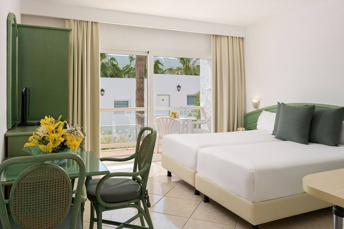 A hotel room with a bed, a desk with a chair, a TV, and a balcony with a table and chairs.