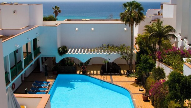 A swimming pool with a view of the ocean, surrounded by buildings and palm trees. - Aparthotel Esquinzo Y Monte Del Mar (Pajara)