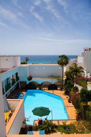 A swimming pool with a view of the ocean, surrounded by buildings and palm trees.