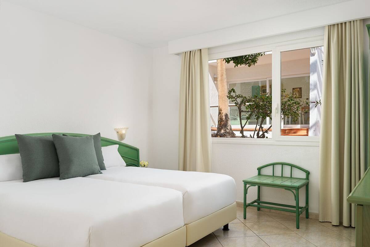 A hotel room with a bed, a chair, a window with curtains, and a view of the outdoors.