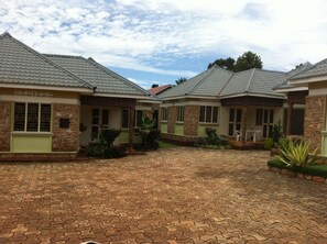 A courtyard with a paved walkway, surrounded by buildings with stone facades and tiled roofs. - Prestige Resort Cottages (Entebbe)