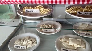 A display case with various types of pasta labeled in Italian. - ElMaima Hotel (Veintiocho de Noviembre)