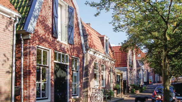 A narrow street lined with traditional brick buildings, a bicycle parked outside, and a dog walking on the sidewalk. - 1 bedroom beach front home in Enkhuizen (Enkhuizen)