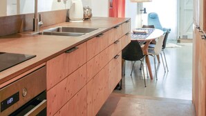A modern kitchen with a stainless steel sink, wooden cabinets, a built-in oven, and a dining area with a round table and chairs. - 1 bedroom beach front home in Enkhuizen (Enkhuizen)