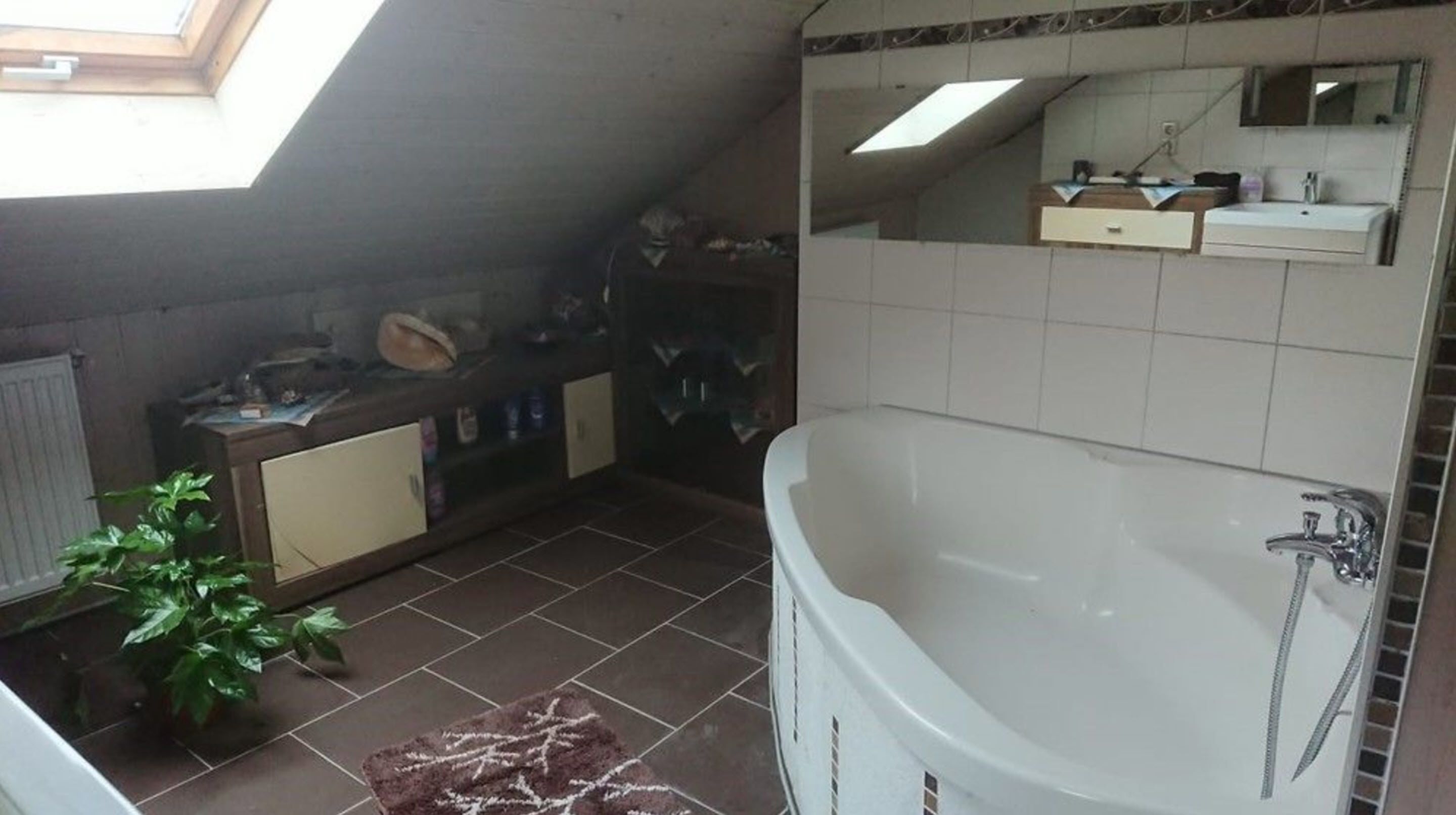 A bathroom with a skylight, a bathtub, a sink, and a mirror.