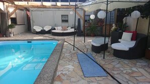 A pool area with stone flooring, a pool, and outdoor seating with cushions and a covered area.