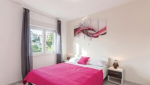 A bedroom with a bed, a nightstand, a window with curtains, and a wall art piece. - Cozy apartment in Podstrana (Podstrana)