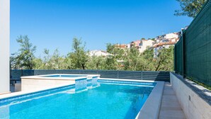 A swimming pool with clear blue water, surrounded by a low stone wall and a metal fence. - Cozy apartment in Podstrana (Podstrana)
