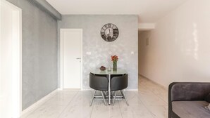 A modern dining area with a glass table, two black chairs, a decorative clock, and a vase with red flowers. - Cozy apartment in Podstrana (Podstrana)
