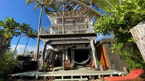 A two-story building with a balcony, surrounded by palm trees and a sandy ground. - Casa Baronesa (Puerto Villamil)