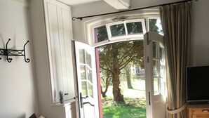 A bedroom with a bed, a desk, a television, and an open door leading to a garden. - Old school ("Godewind" from "Gegen den Wind") Sankt Peter Ording village - studio (St. Peter-Ording)