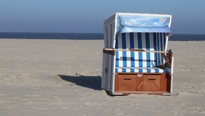A beach chair with a striped cushion and a canopy, positioned on a sandy beach with the ocean in the background. - Old school ("Godewind" from "Gegen den Wind") Sankt Peter Ording village - studio (St. Peter-Ording)