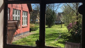 A view through a window with a thatched roof house, a grassy yard, and a wooden bench. - Old school ("Godewind" from "Gegen den Wind") Sankt Peter Ording village - studio (St. Peter-Ording)