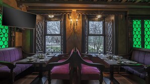 Un restaurante con una mesa central, asientos morados y ventanas iluminadas en verde.