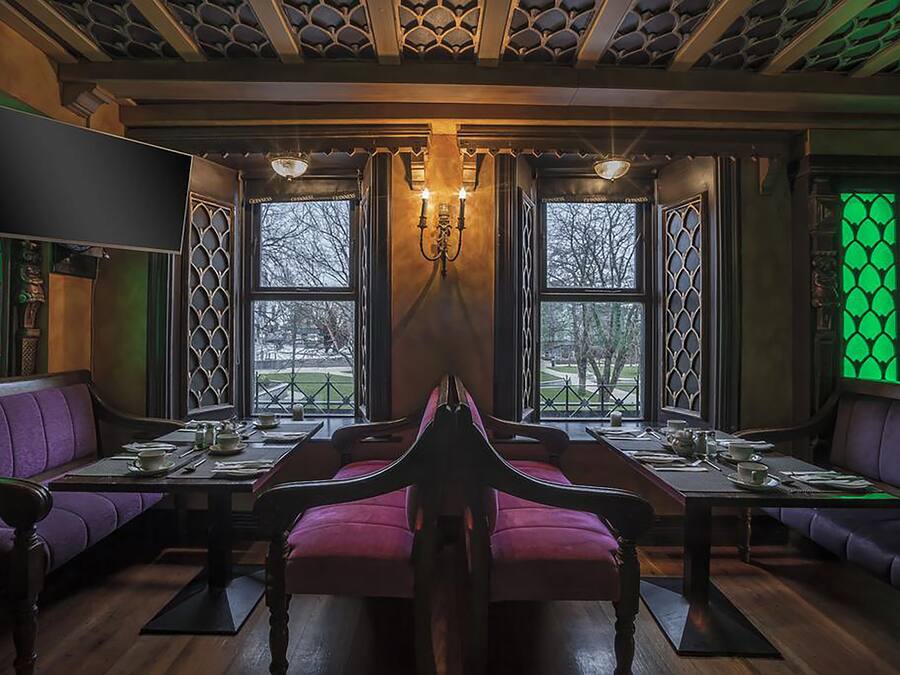 Un restaurante con una mesa central, asientos morados y ventanas iluminadas en verde.