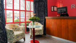 Un área de recepción con dos sillones estampados, una mesa de vidrio y un mostrador de madera.