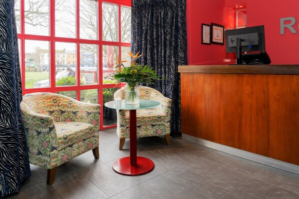 Un área de recepción con dos sillones estampados, una mesa de vidrio y un mostrador de madera.