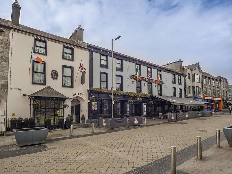 Un hôtel avec une porte rouge, une enseigne indiquant « HÔTEL », et un pub appelé « THE SKEEP » situé de l’autre côté de la rue.