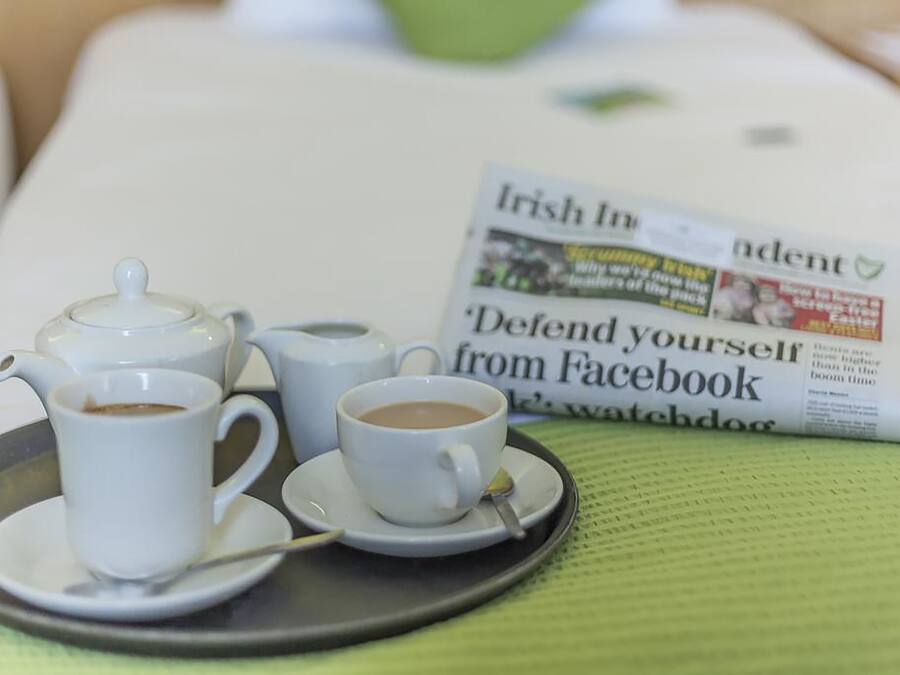 Ein Tablett mit Kaffeetassen und einem Teekessel auf einem Tisch, im Hintergrund eine Zeitung mit der Überschrift 'Irish Independent'.