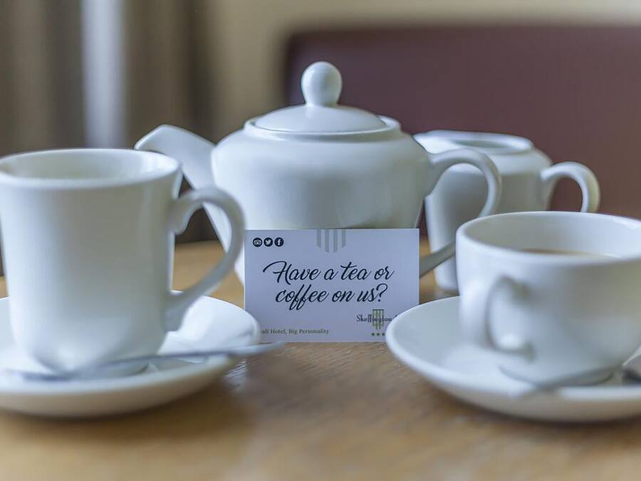 Una mesa con tazas blancas, una tetera y un letrero que pregunta si se desea té o café.