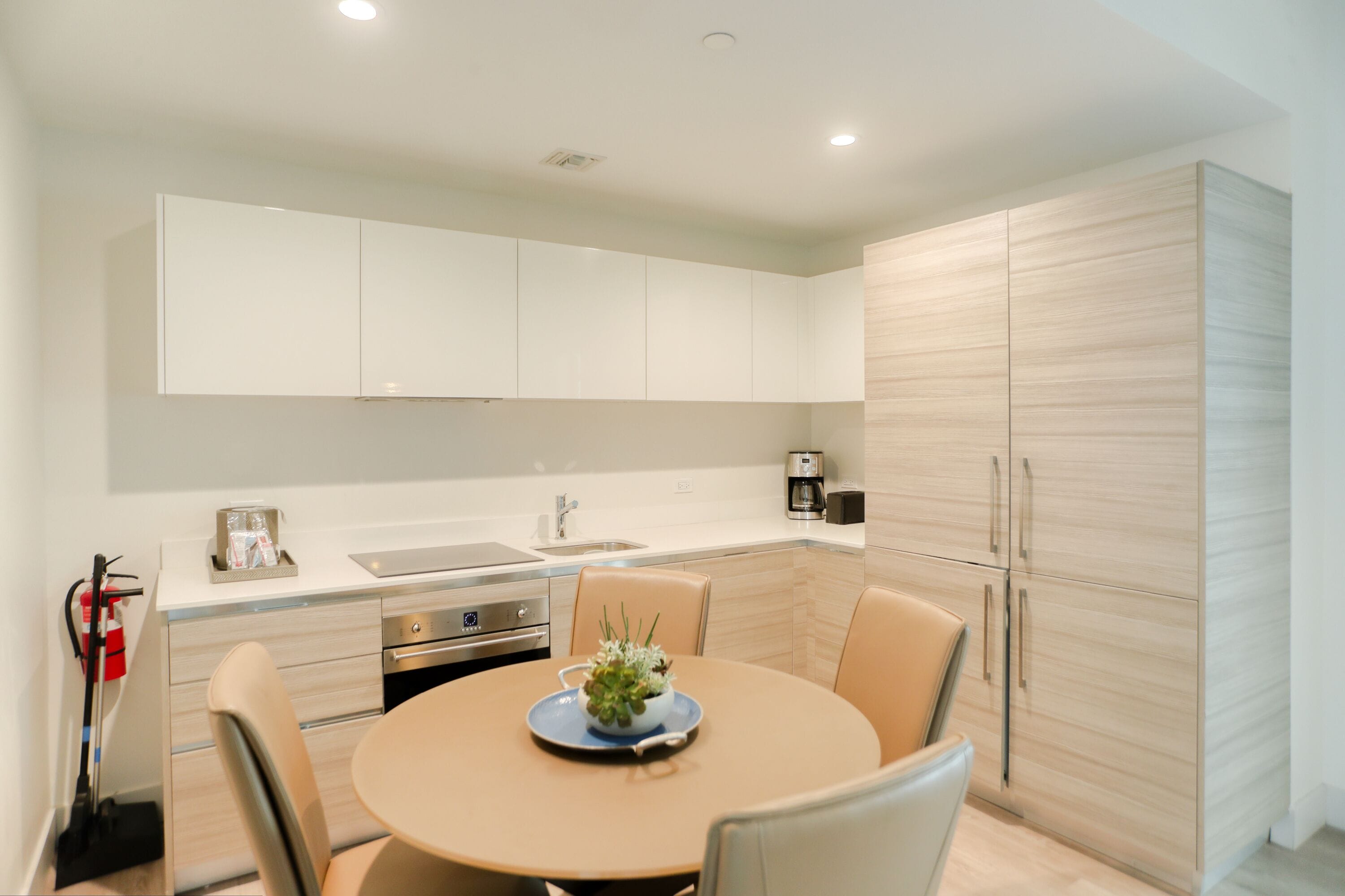A modern kitchen with white cabinets, a built-in oven, and a round dining table with chairs.