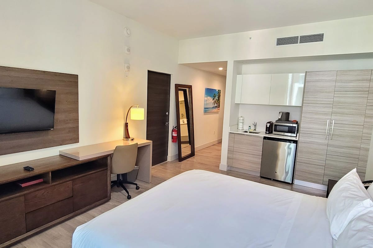 Une chambre d’hôtel équipée d’un lit, d’un bureau, d’une télévision, d’une kitchenette et d’un miroir.