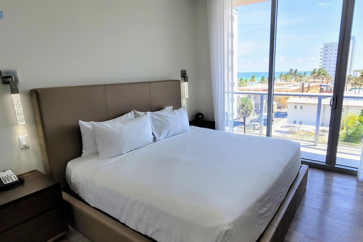 Une chambre d’hôtel avec un grand lit, un téléphone sur la table de chevet et une vue sur la plage et la ville par la fenêtre.